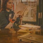 About A woman enjoys reading while sipping wine in a cozy Ankara café. Warm ambience.